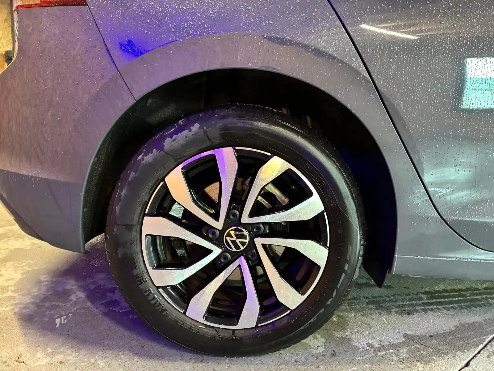 Gros plan sur la roue arrière droite d’une Volkswagen Golf gris 2022, avec jante alliage bicolore et carrosserie mouillée.