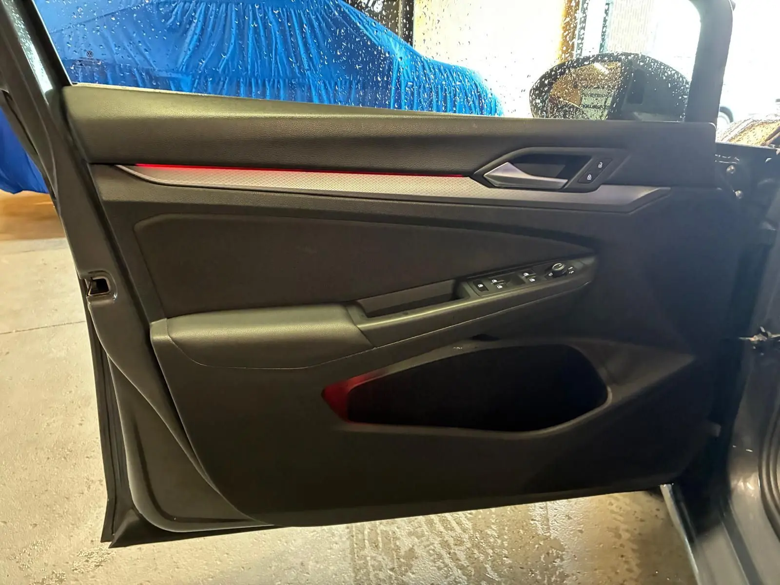 Vue intérieure côté gauche de la porte avant d’une Volkswagen Golf gris 1.5 eTSI 130 DSG7 avec éclairage d’ambiance rouge.