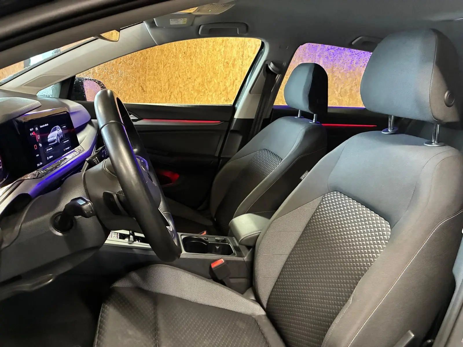 Intérieur avant de la Volkswagen Golf 1.5 eTSI 130 DSG7 Active 2022, vue côté conducteur, sièges tissu noir et éclairage d’ambiance rouge.