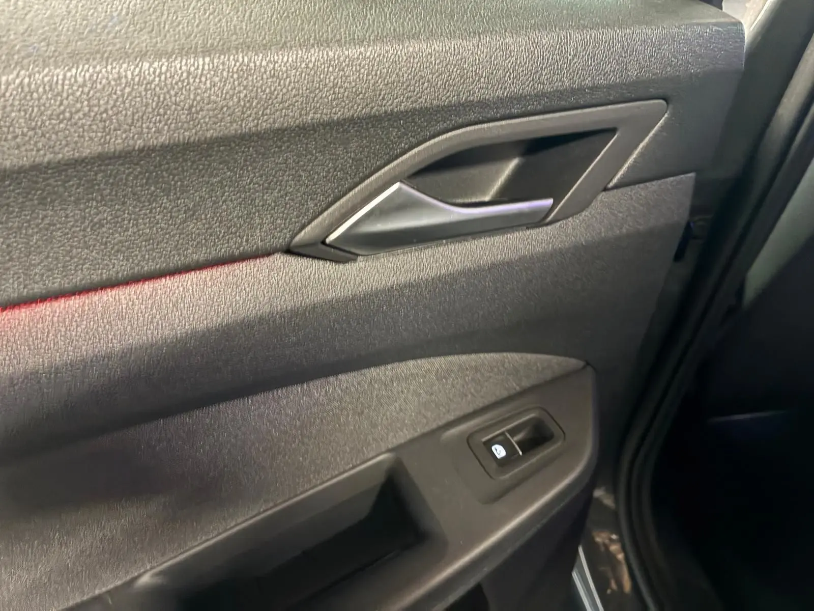 Détail de la porte intérieure côté droit de la Volkswagen Golf gris, avec poignée argentée et bouton de lève-vitre.