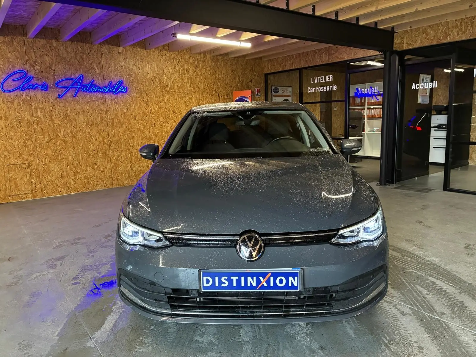 Vue de face d'une Volkswagen Golf 1.5 eTSI gris métallisé 2022, avec phares LED allumés dans un showroom intérieur.