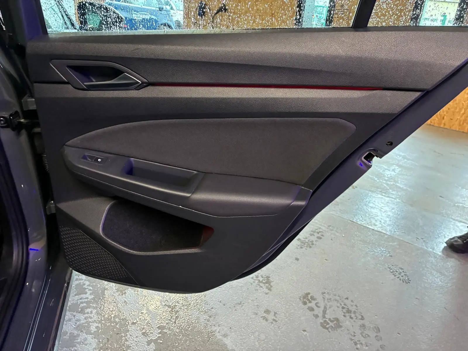 Vue intérieure de la porte arrière droite d'une Volkswagen Golf gris 2022 avec garniture noire et éclairage d'ambiance rouge.