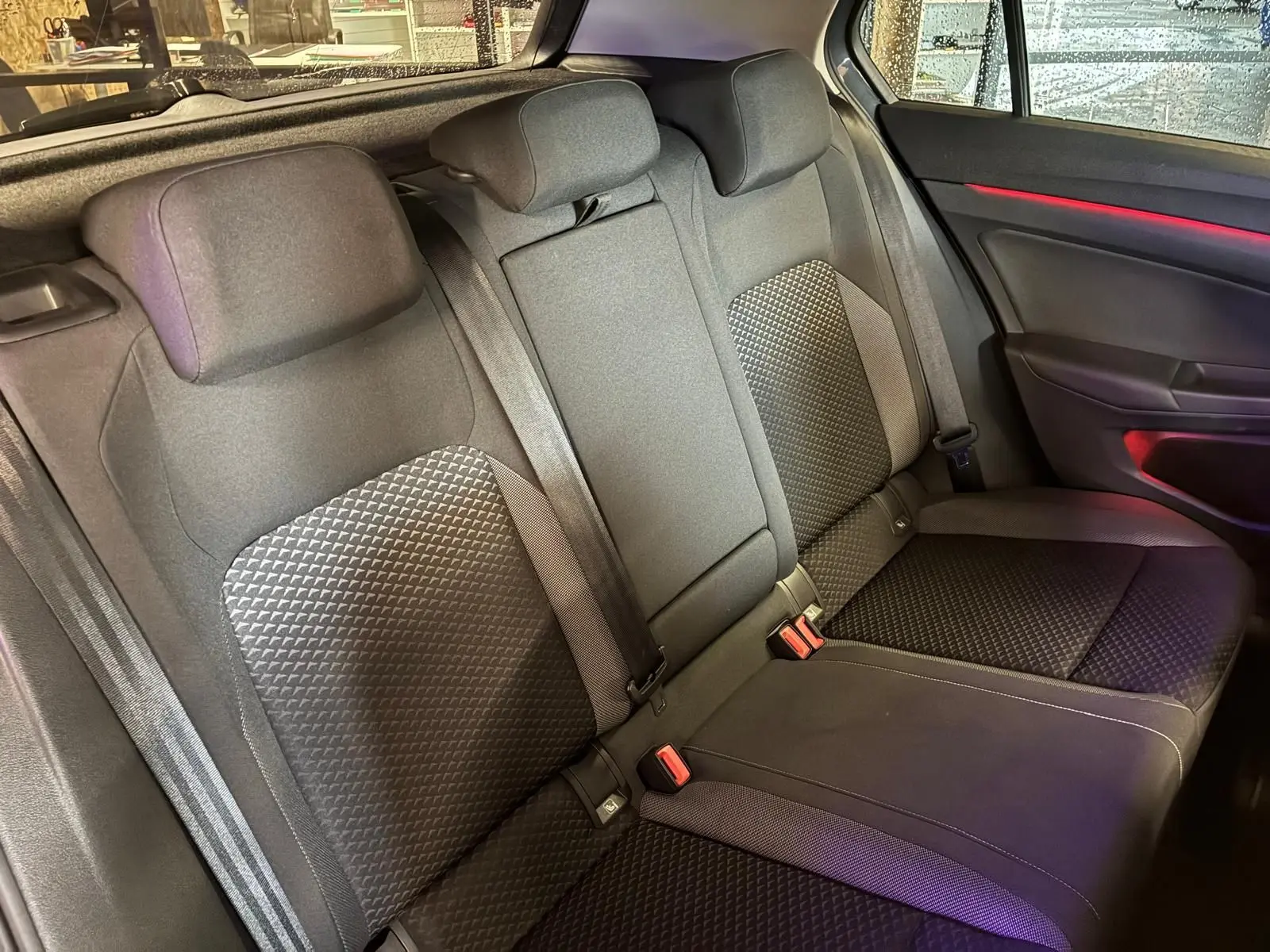 Vue intérieure sur la banquette arrière en tissu noir avec motifs géométriques et éclairage d'ambiance rouge côté droit.