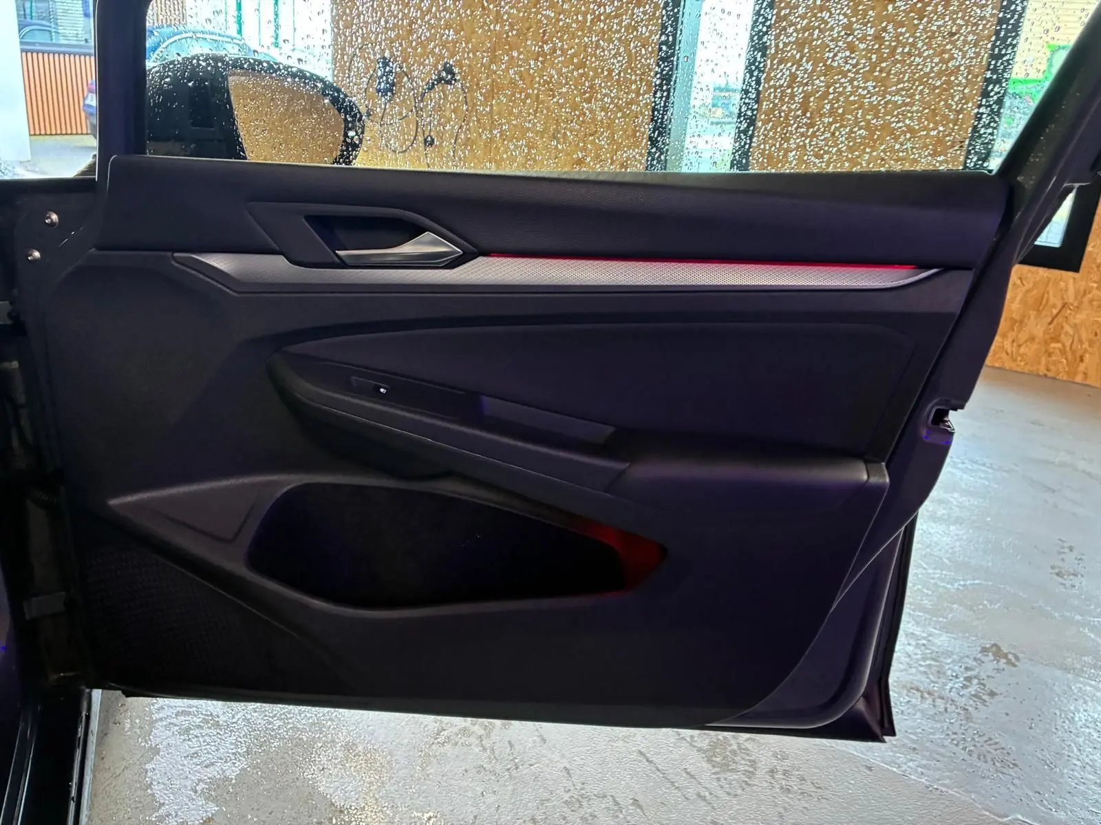 Vue intérieure de la porte avant gauche de la Volkswagen Golf gris, avec éclairage d'ambiance rouge et insert décoratif.