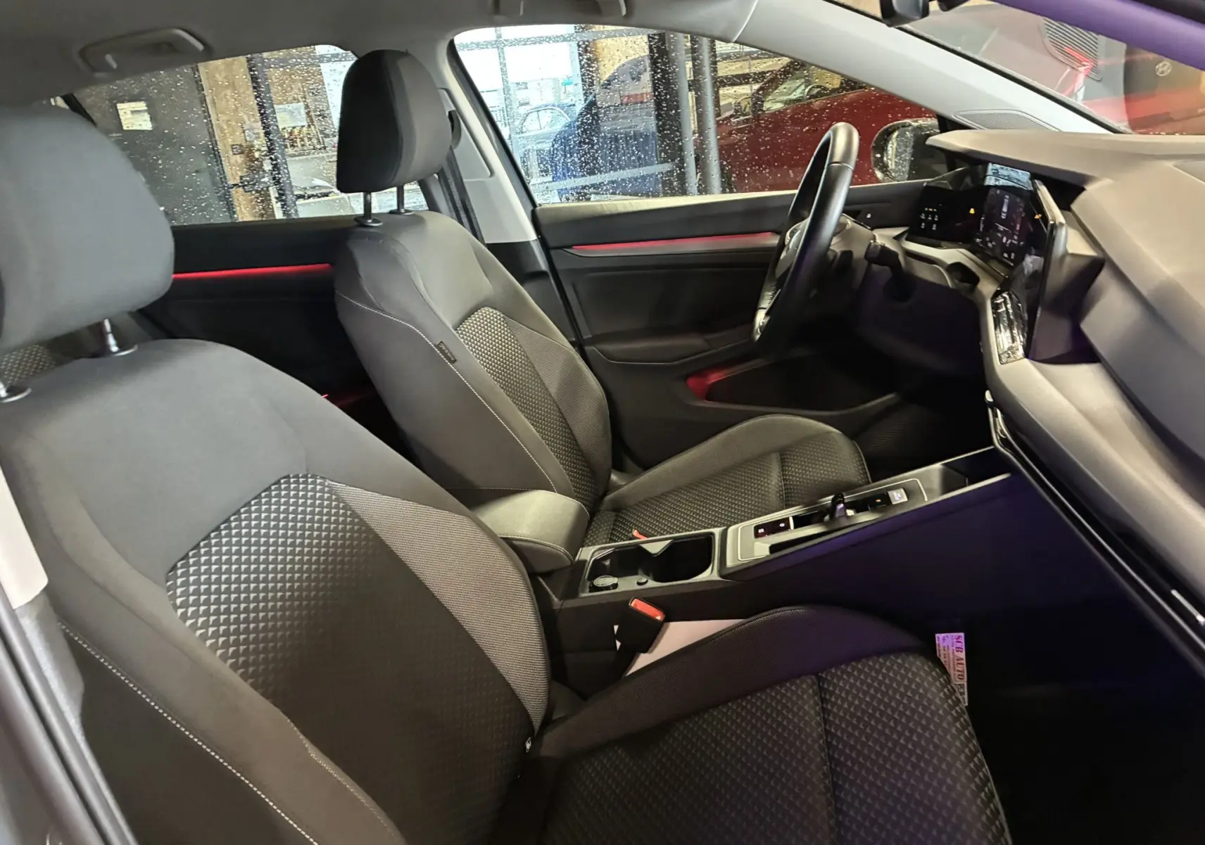 Vue intérieure côté conducteur de la Volkswagen Golf 1.5 eTSI 130 DSG7 Active 2022 avec sièges tissu noir et éclairage d'ambiance rouge.