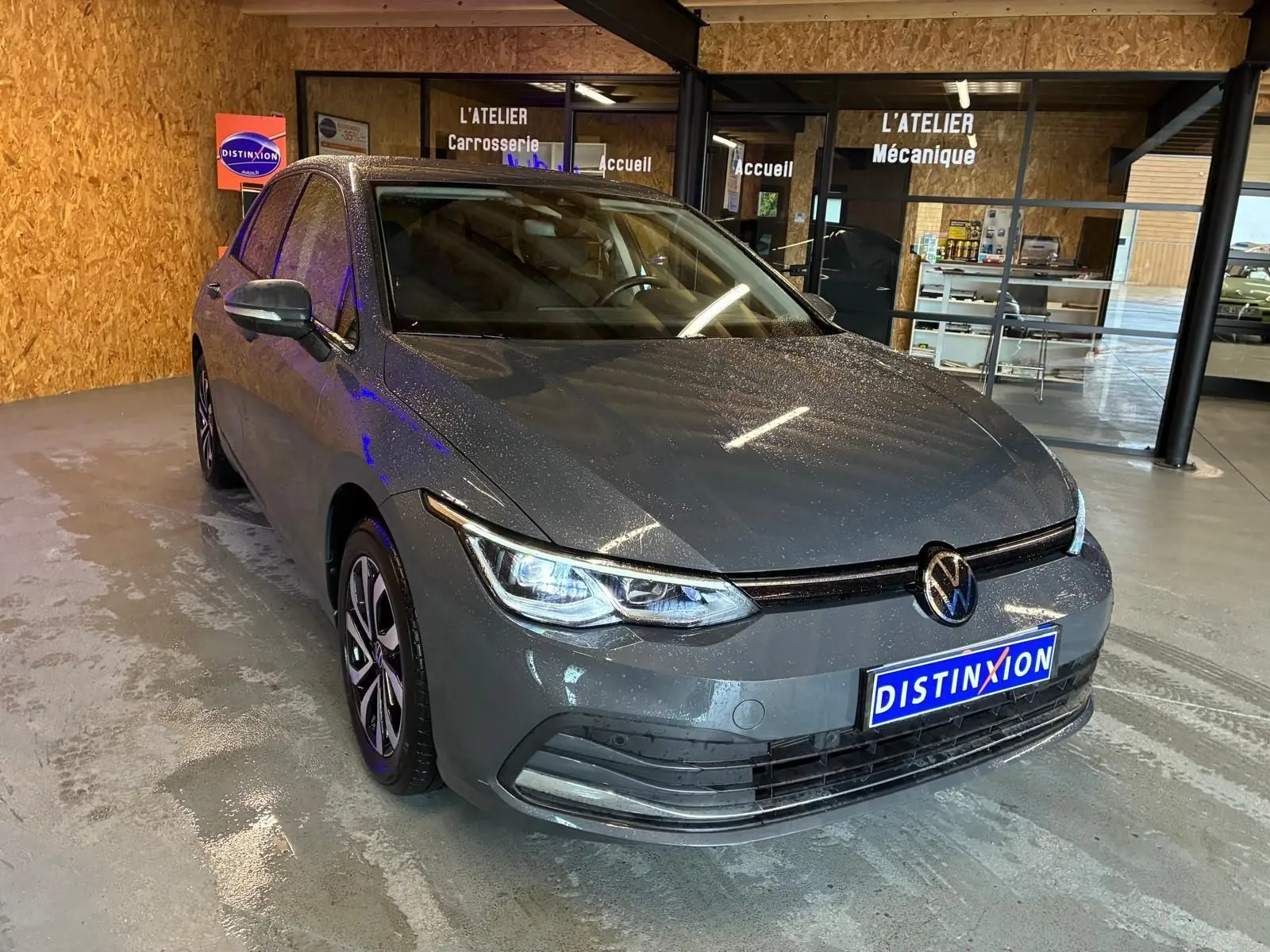 Vue 3/4 avant d'une Volkswagen Golf gris métallisé 2022 avec phares allumés dans un atelier automobile.