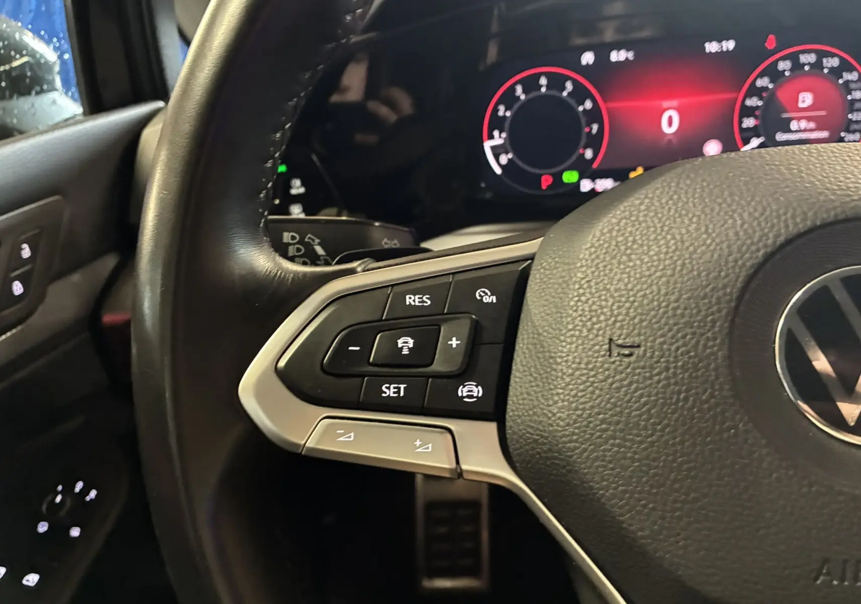 Gros plan sur le volant noir de la Volkswagen Golf 1.5 eTSI 130 DSG7 Active avec commandes intégrées et tableau de bord numérique rouge.