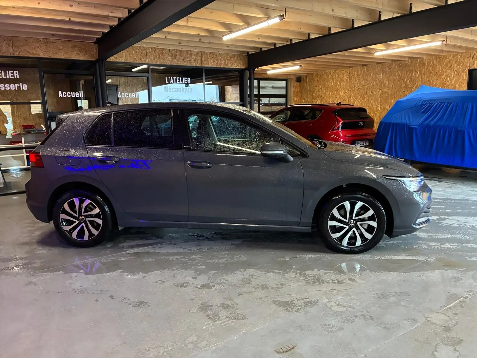 Vue de profil côté gauche d'une Volkswagen Golf gris métallisé 2022 stationnée en intérieur avec jantes distinctives.