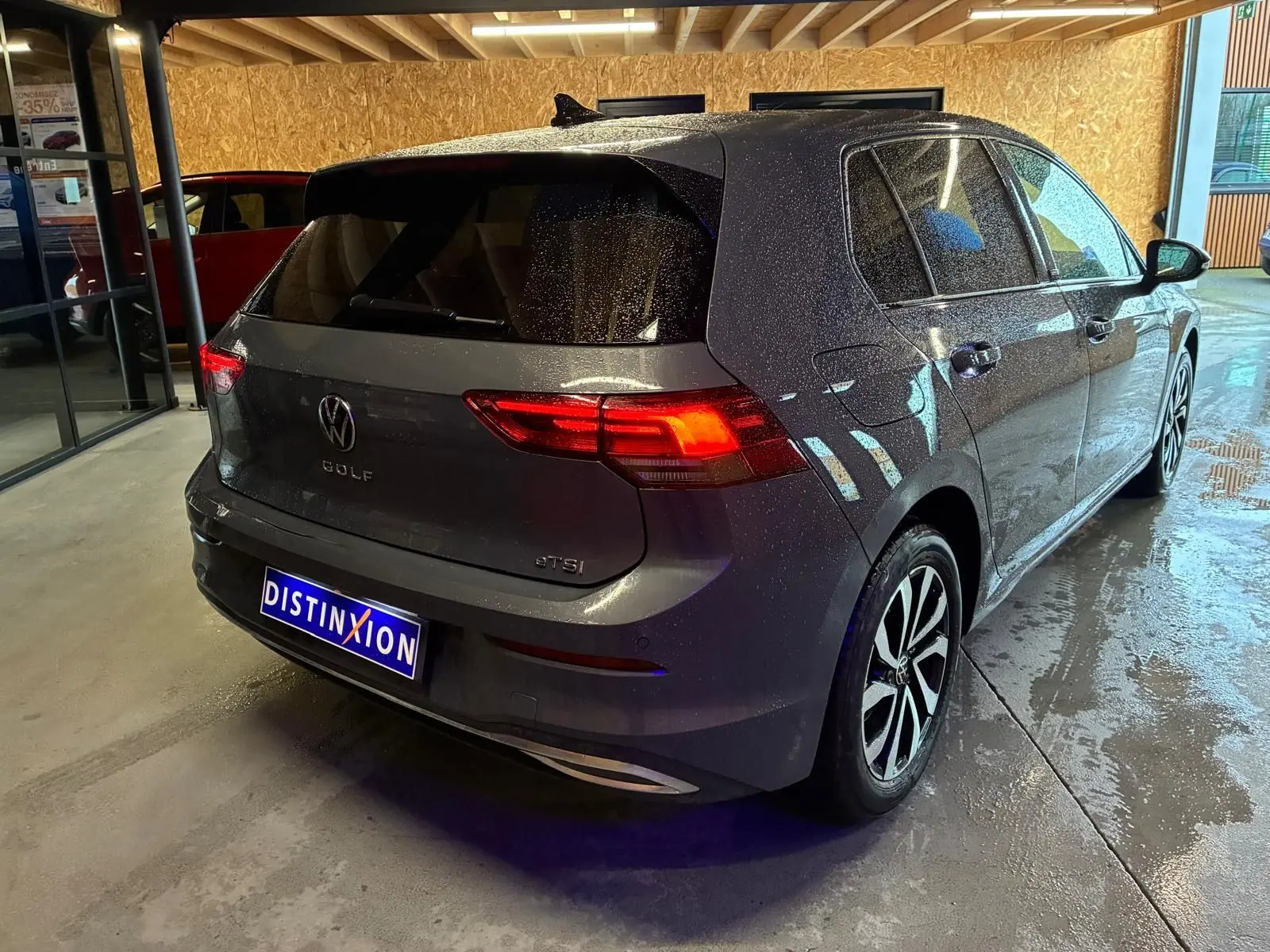 Vue 3/4 arrière droite d'une Volkswagen Golf gris métallisé 5 portes avec feux arrière allumés en intérieur showroom.