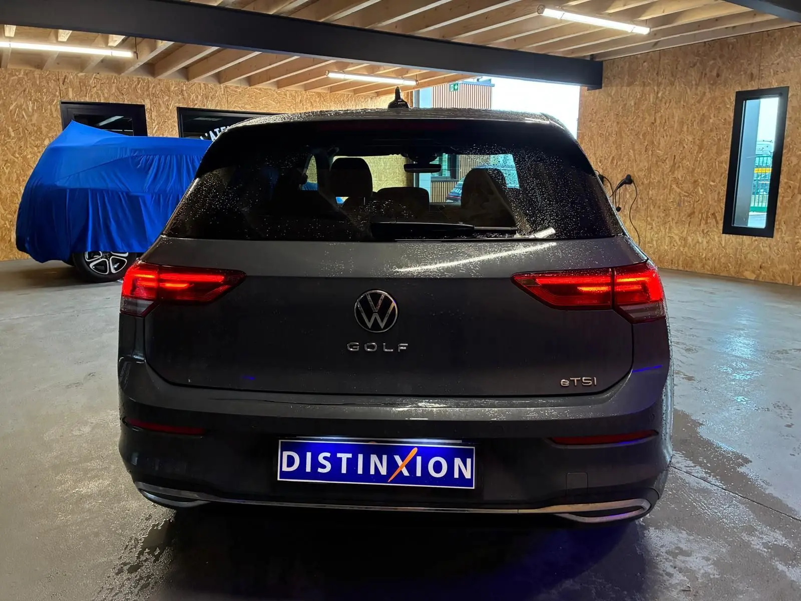 Vue arrière d'une Volkswagen Golf gris foncé 1.5 eTSI 130 DSG7 ACTIVE avec feux arrière allumés en intérieur.