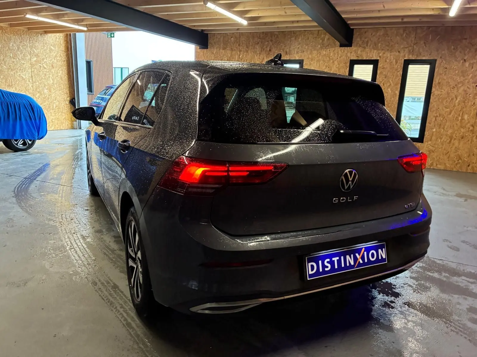Vue 3/4 arrière droite d'une Volkswagen Golf gris foncé 1.5 eTSI 130 DSG7 Active avec feux arrière allumés en intérieur.