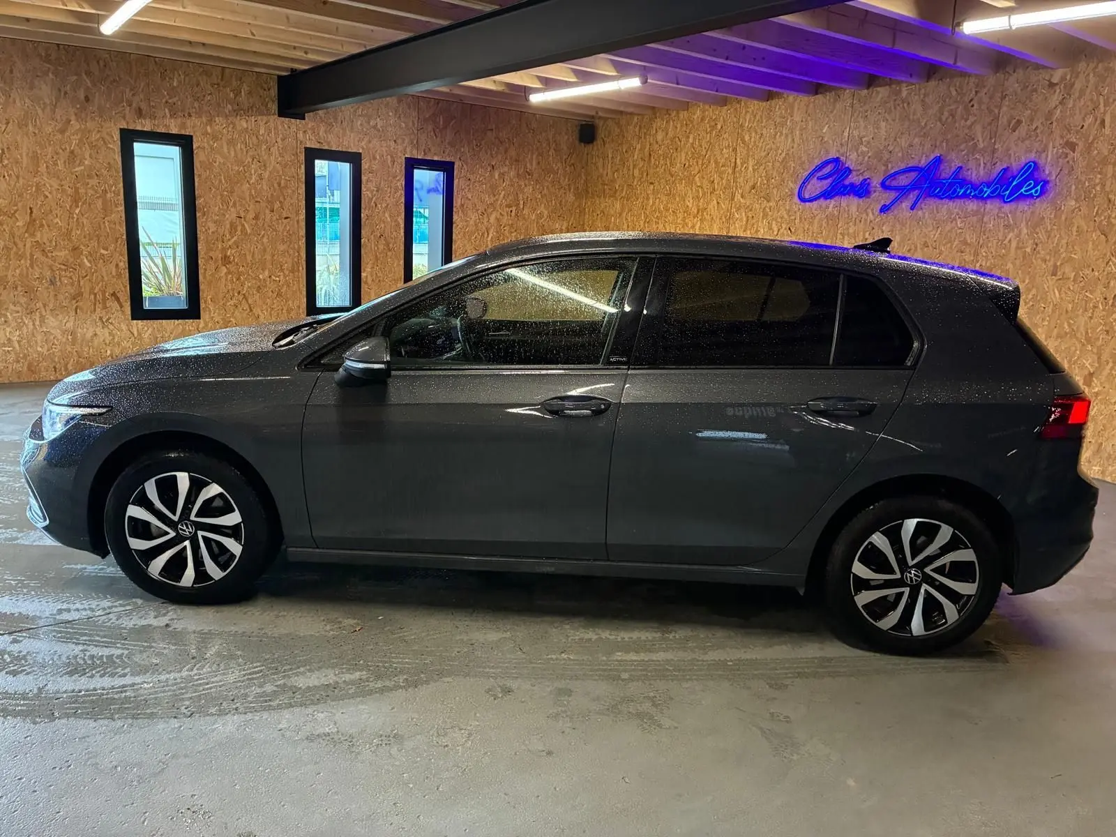 Vue de profil côté gauche d'une Volkswagen Golf gris métallisé 5 portes, stationnée en intérieur avec éclairage néon bleu.
