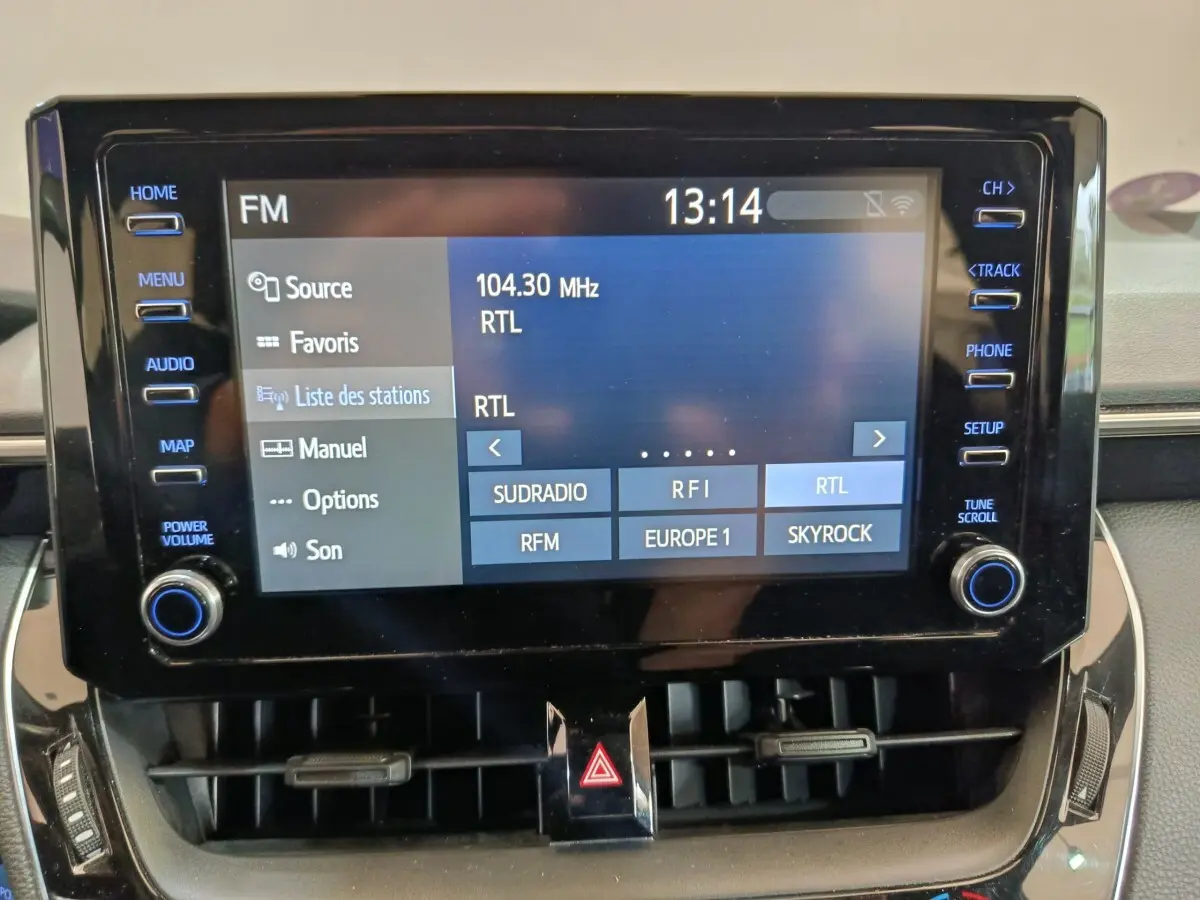 Écran tactile central de la Toyota Corolla Hybride 2020 affichant les stations radio FM, entouré de boutons de commande.