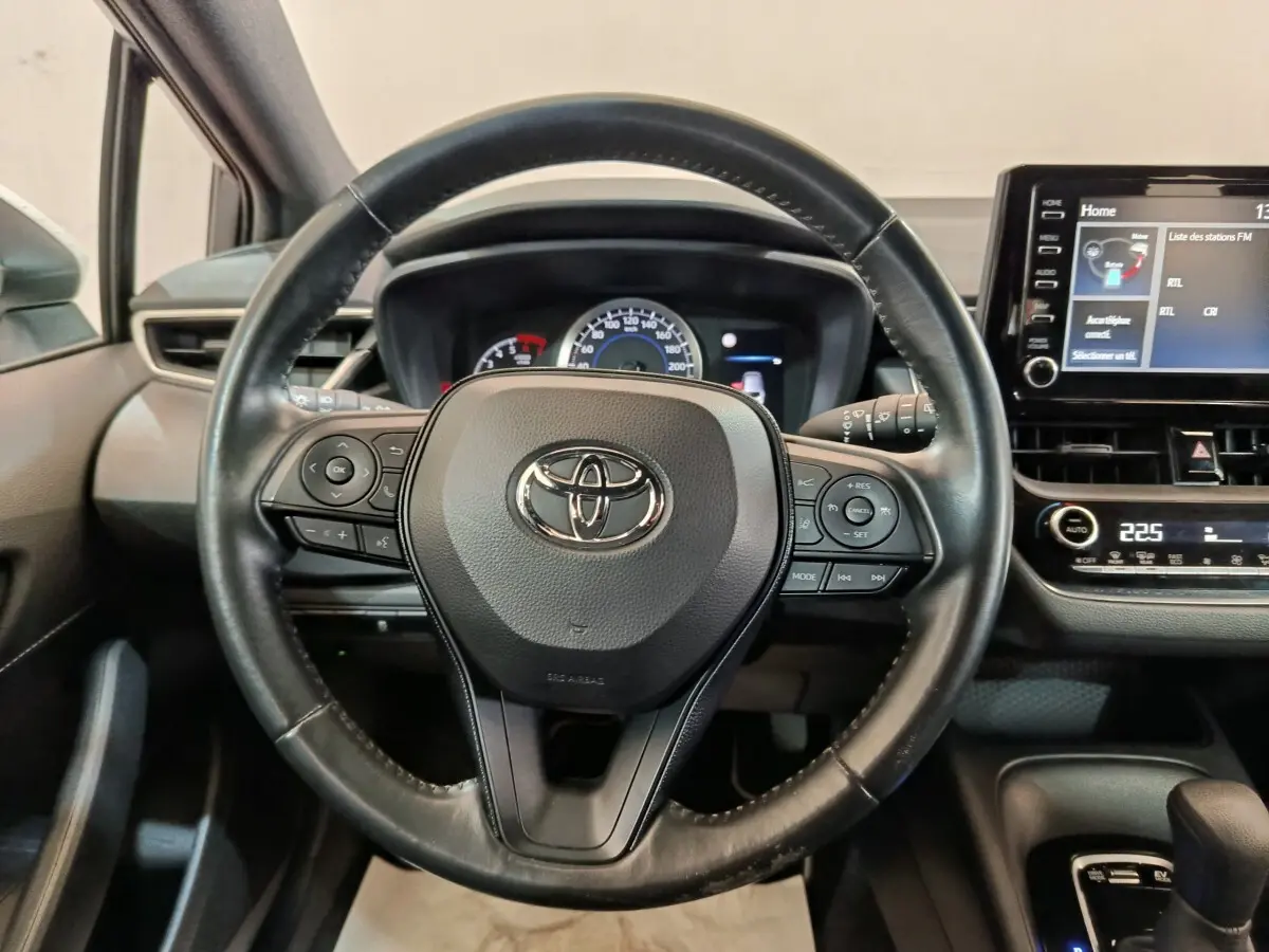 Vue rapprochée du volant cuir noir de la Toyota Corolla Hybride 122h 2020 avec tableau de bord et écran tactile visible.