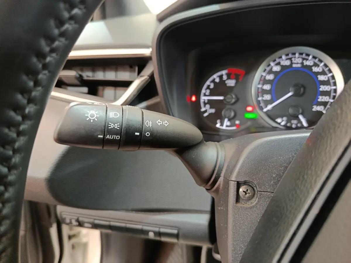 Gros plan sur la manette des phares et clignotants à gauche du volant dans le tableau de bord d'une Toyota Corolla hybride.