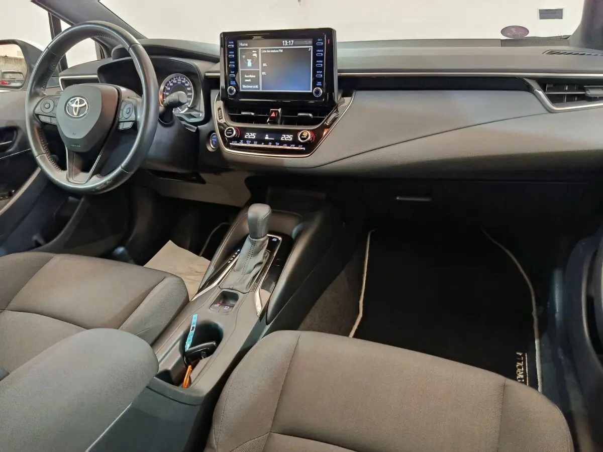 Intérieur de la Toyota Corolla Hybride 122h 2020 vu côté conducteur, tableau de bord noir avec écran tactile central et console centrale.