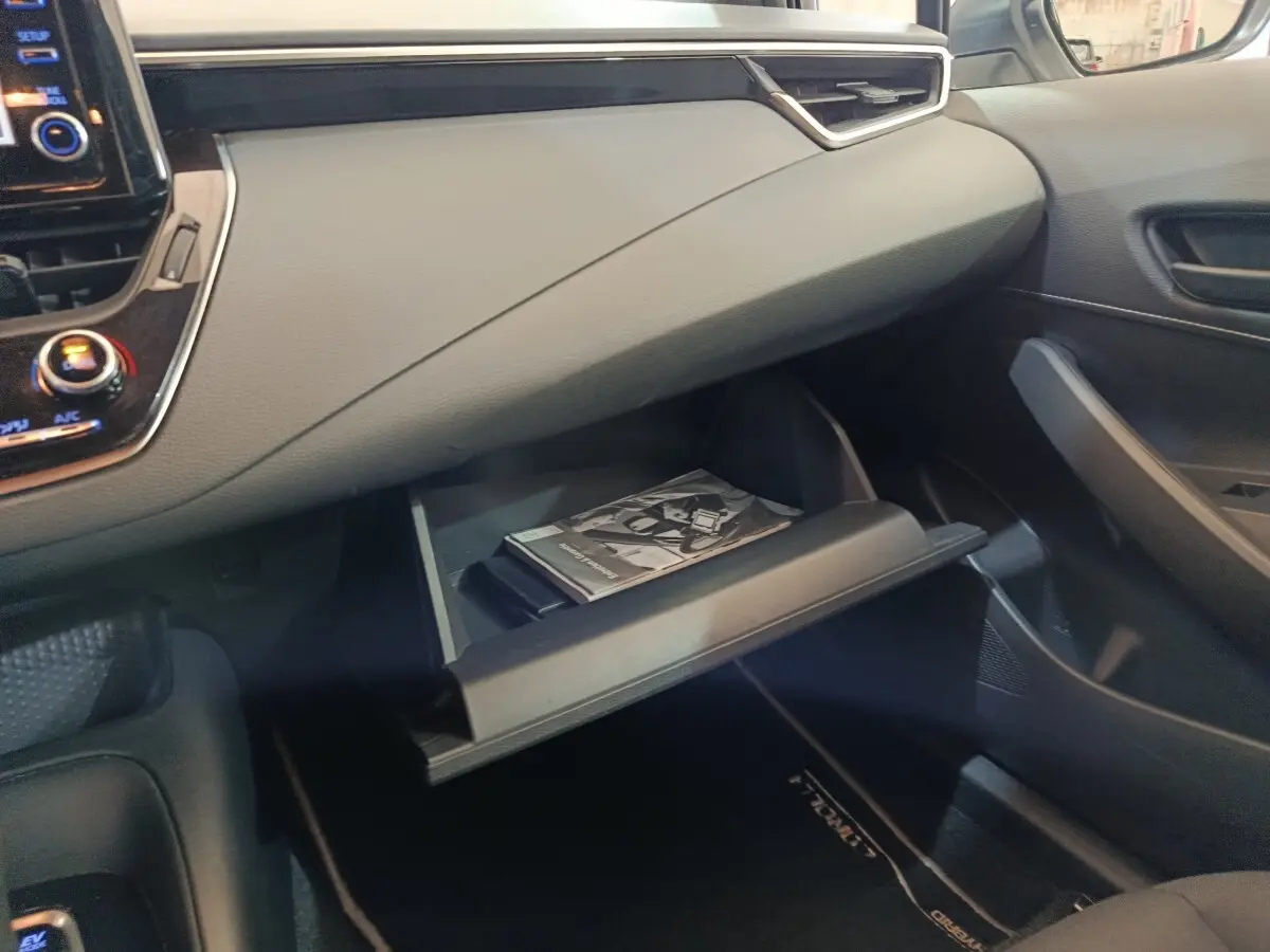 Vue intérieure côté passager de la boîte à gants ouverte de la Toyota Corolla Hybride 122h Active avec manuel visible.