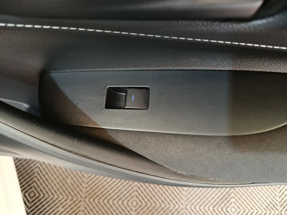 Gros plan sur le bouton de commande de lève-vitre côté porte intérieure noire de la Toyota Corolla Hybride blanche 2020.