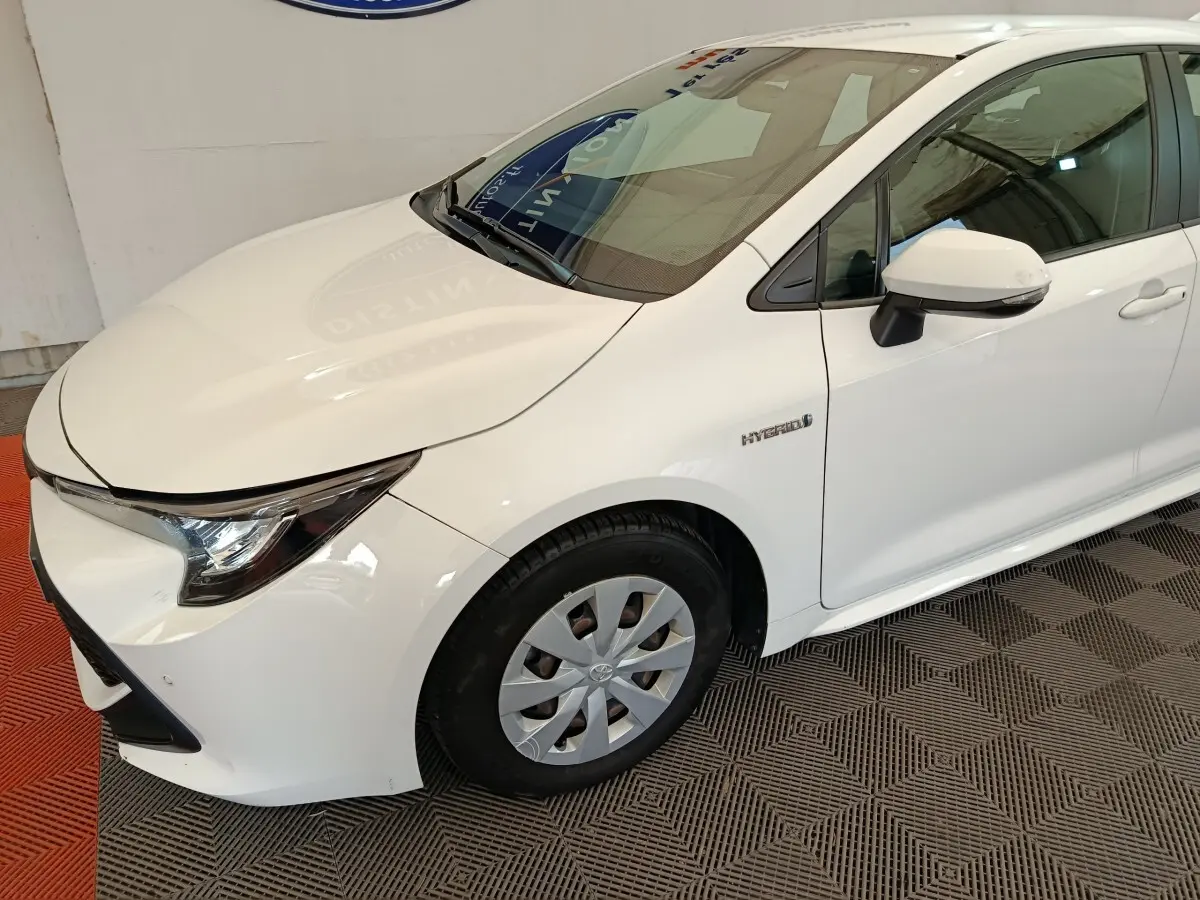 Vue 3/4 avant droit d'une Toyota Corolla Hybride 122h Active blanche, avec badge Hybrid visible sur l'aile avant.