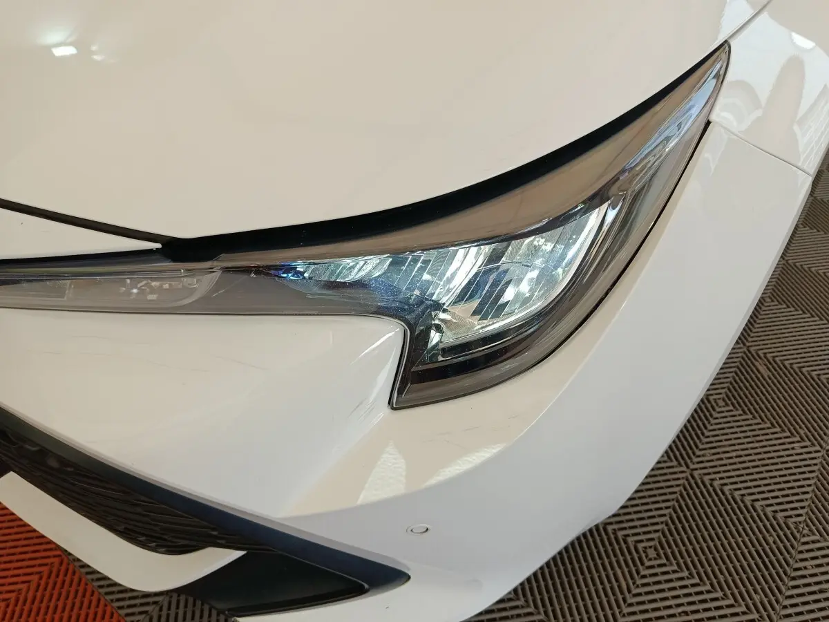 Gros plan sur le phare avant droit blanc d'une Toyota Corolla Hybride 122h Active 2020, avec détails du pare-chocs.