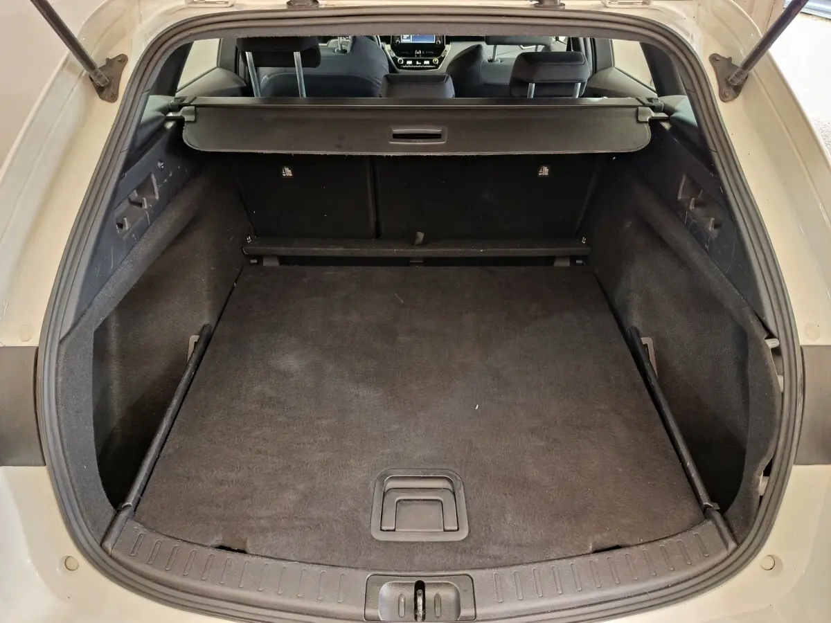 Coffre ouvert vu de l'arrière d'une Toyota Corolla Hybride blanche, avec cache-bagages en place et intérieur noir.