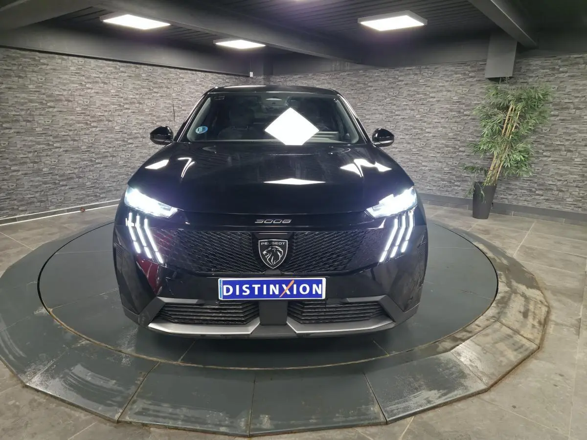 Vue avant d'un Peugeot 3008 noir 2025 avec feux LED à 3 griffes et calandre noire laquée dans un showroom.