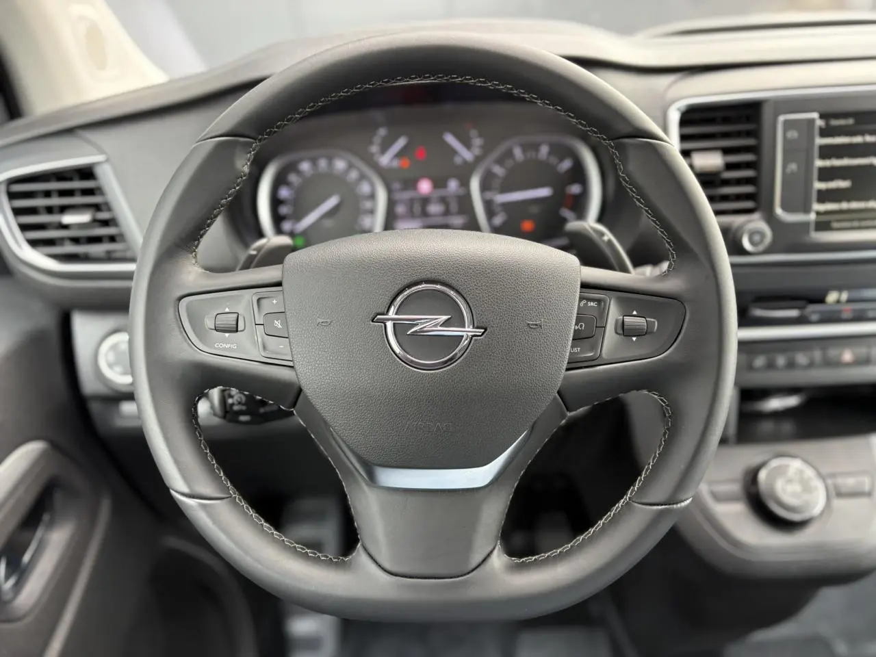 Volant en cuir noir avec logo Opel au centre, tableau de bord et écran tactile visibles en arrière-plan.