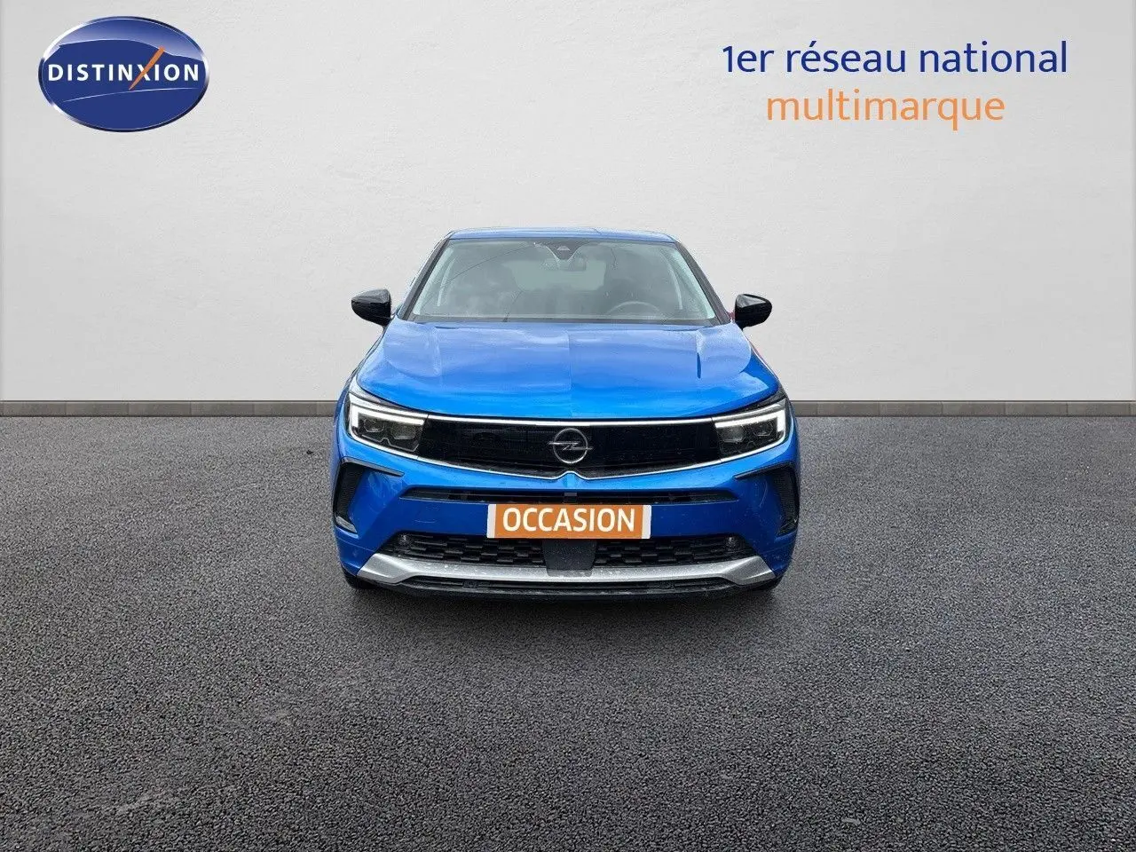 Vue frontale d'un Opel Grandland bleu Spektrum Metal avec plaque "OCCASION" sur un sol gris.