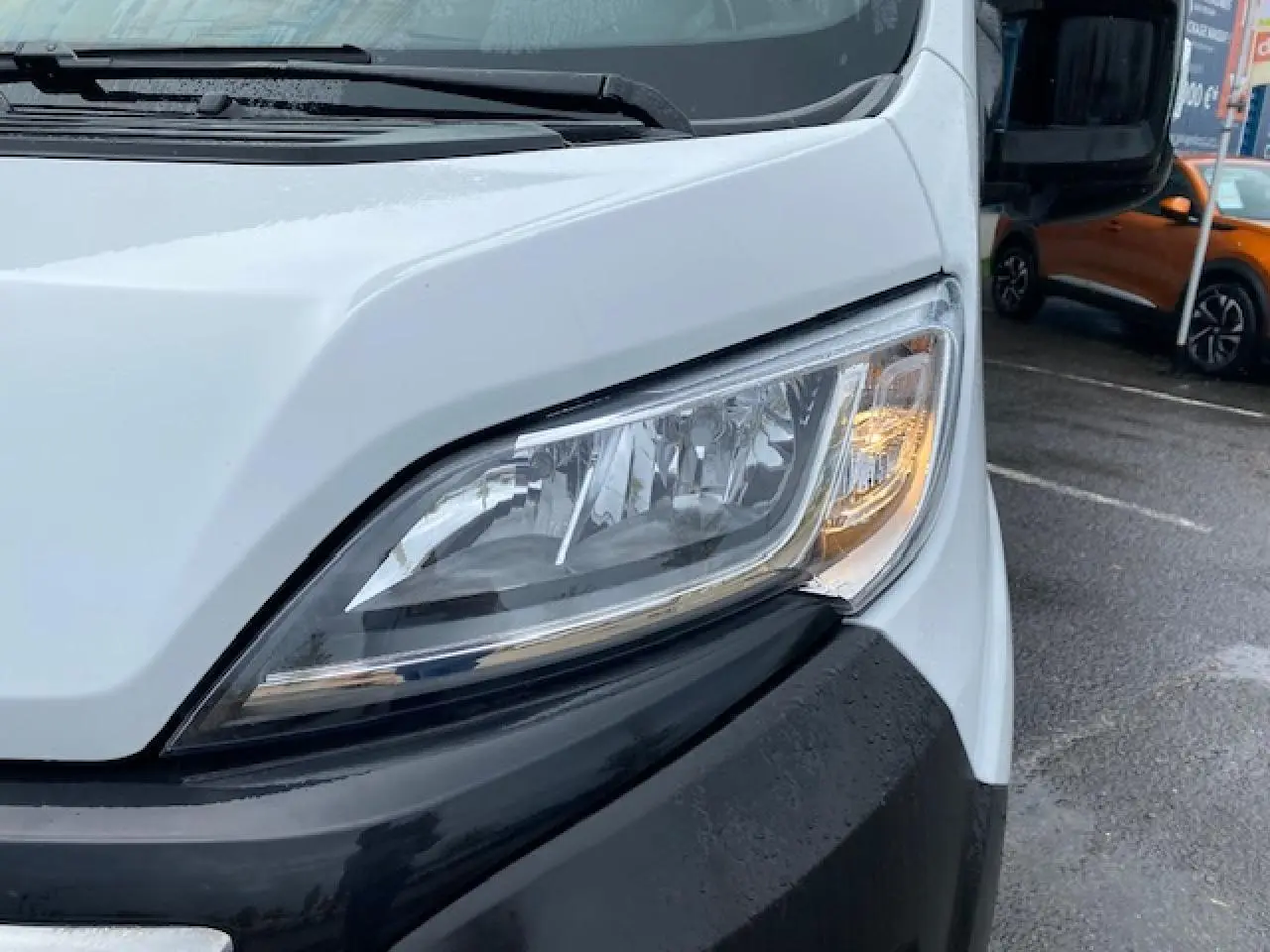 Gros plan sur le phare avant droit du fourgon blanc Opel Movano 2023, soulignant le pare-chocs noir et la carrosserie lisse.