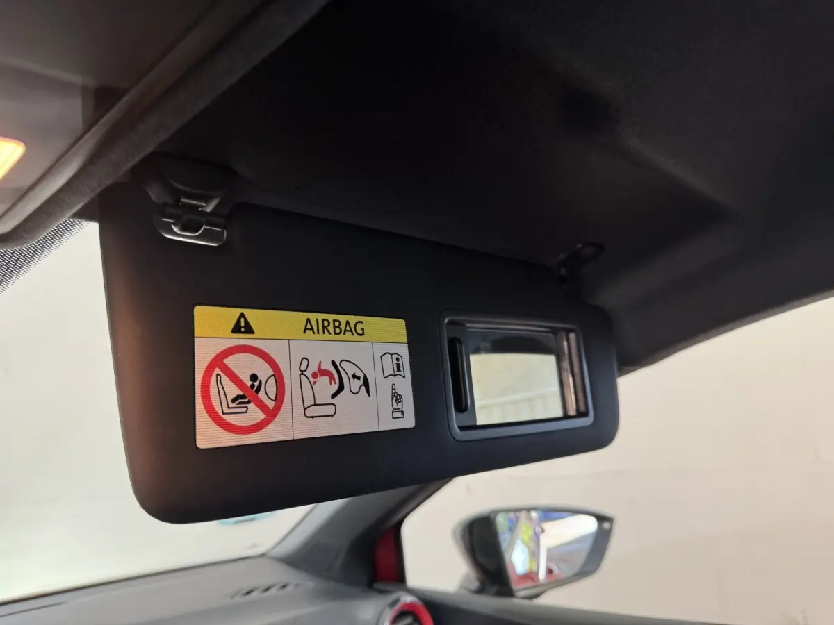 Vue intérieure du pare-soleil côté conducteur avec miroir et avertissement airbag, rétroviseur extérieur rouge visible.