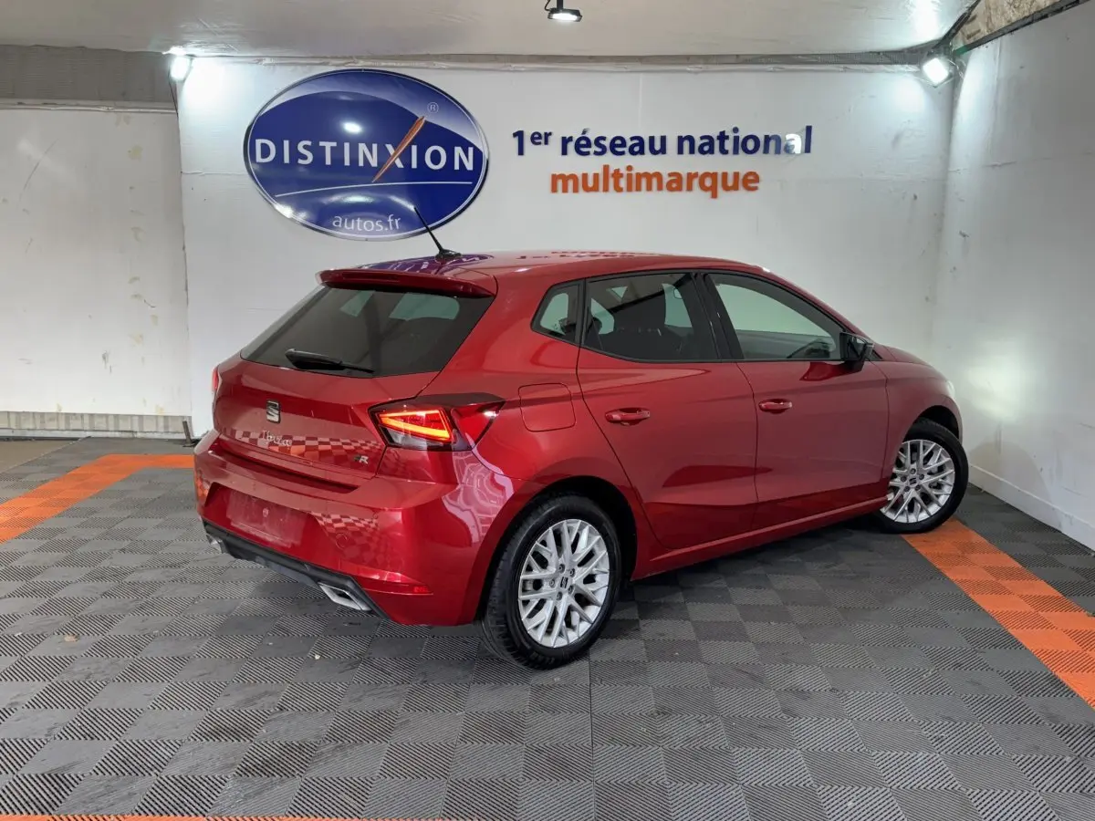 Vue 3/4 arrière droite d'une SEAT Ibiza 1.0 TSI 110 FR rouge brillante avec jantes alliage et feux LED allumés.