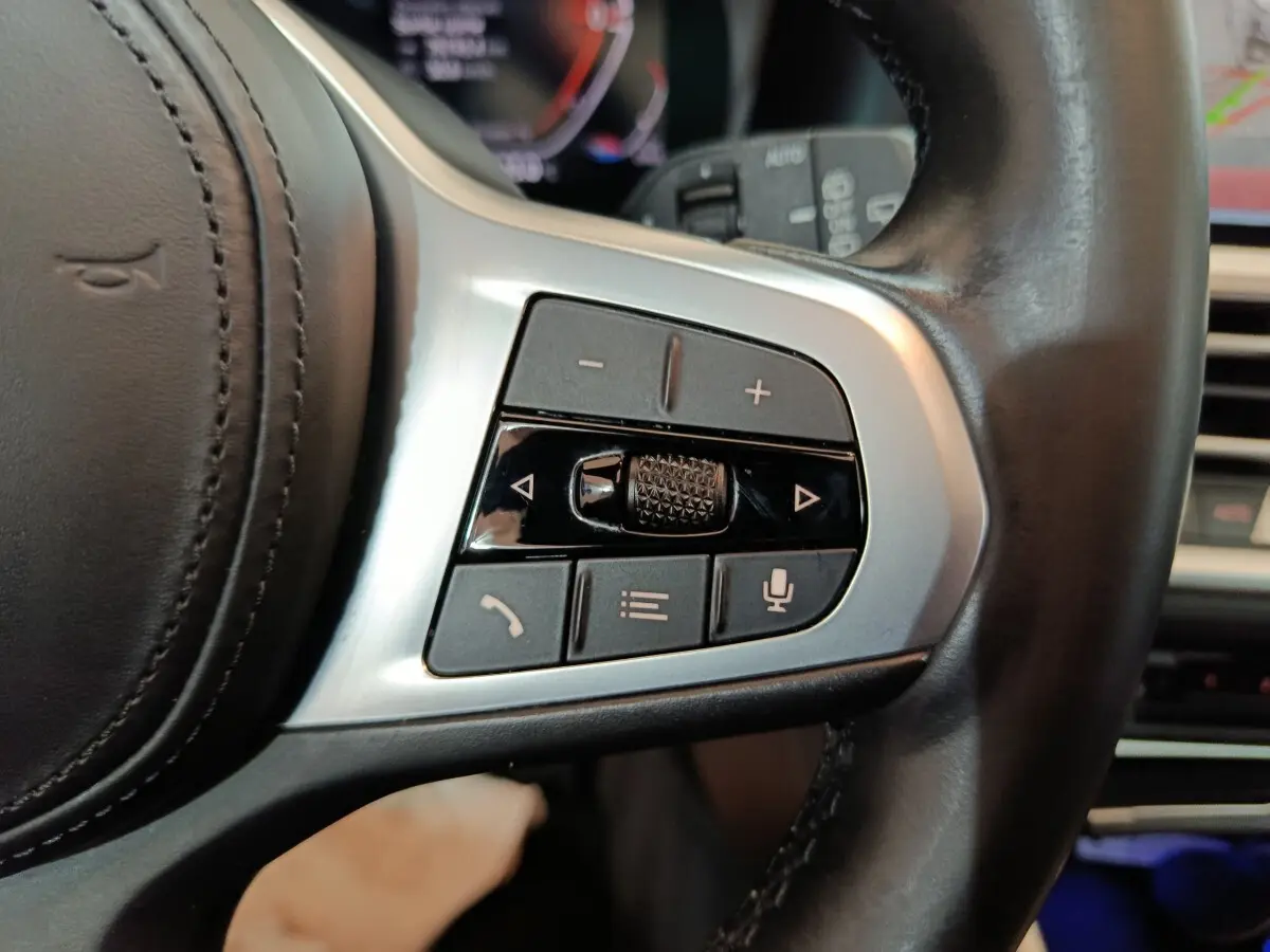 Gros plan sur les commandes multifonctions argentées du volant cuir noir d'une BMW Série 3 318d 2022.