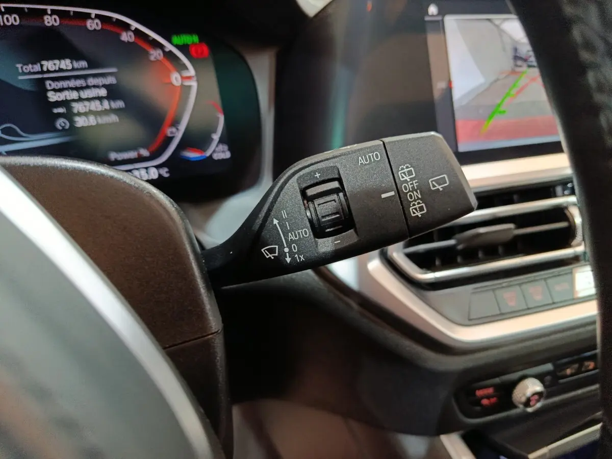 Gros plan sur la manette d'essuie-glace côté gauche du tableau de bord d'une BMW Série 3 gris clair, avec affichage numérique en arrière-plan.
