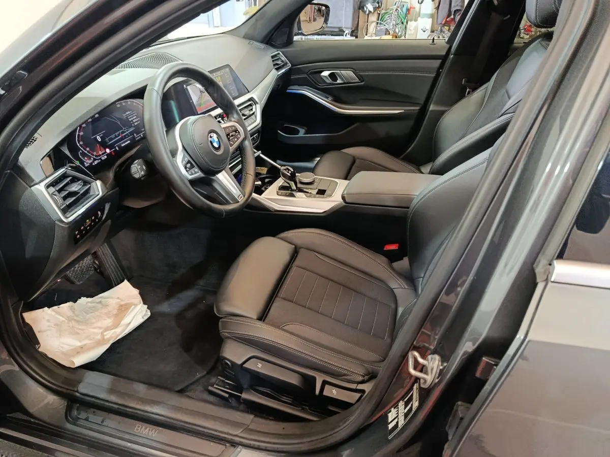 Vue intérieure côté conducteur de la BMW Série 3 318d grise, avec sièges cuir noirs et tableau de bord digital.