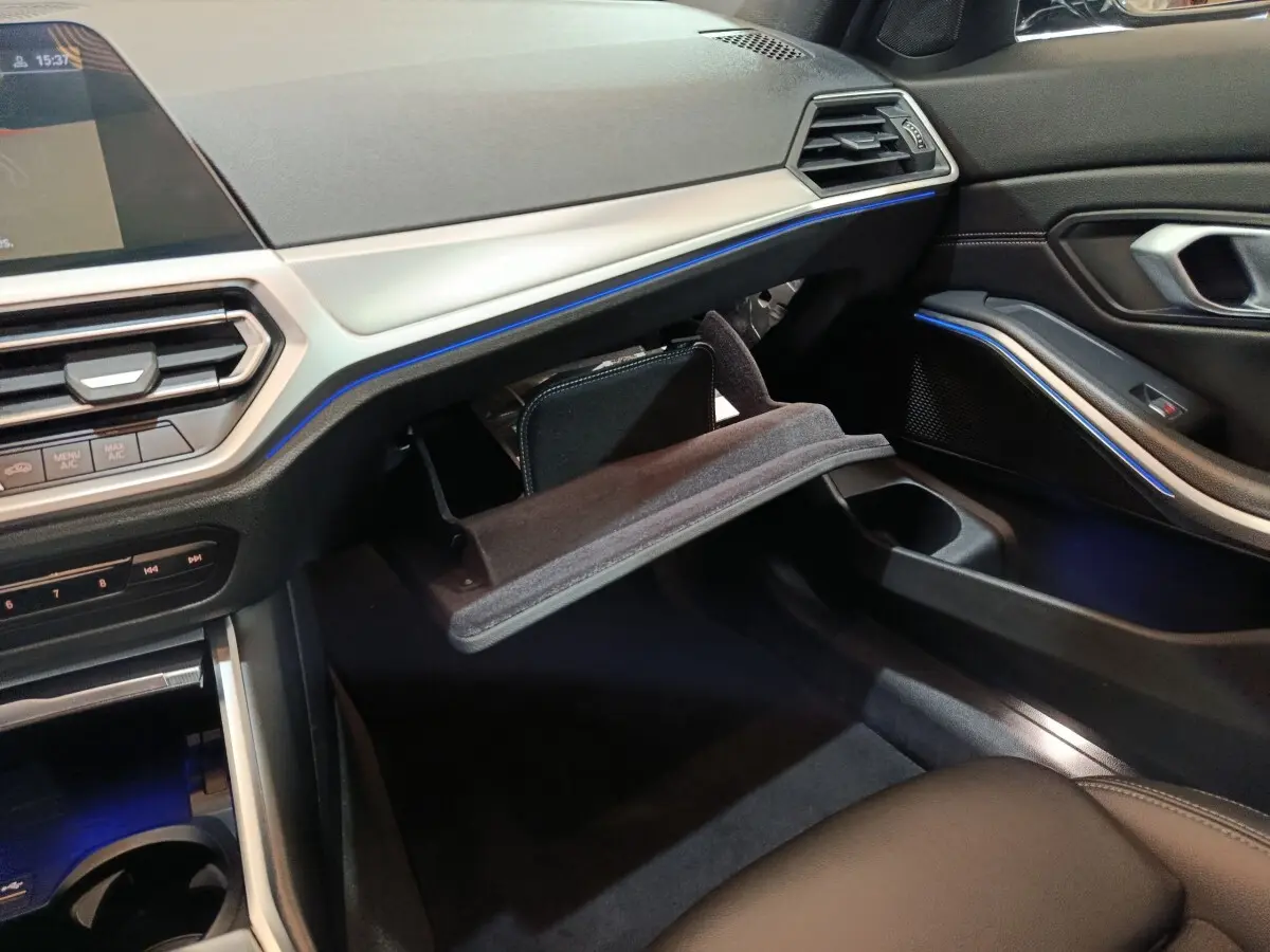 Intérieur BMW Série 3 318d 2022, vue côté passager avec boîte à gants ouverte et éclairage d’ambiance bleu.