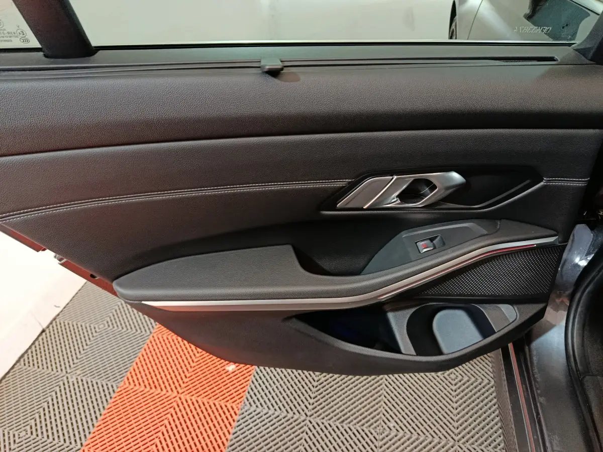 Vue intérieure côté droit de la porte d’une BMW Série 3 gris clair, avec garniture noire et poignée métal.