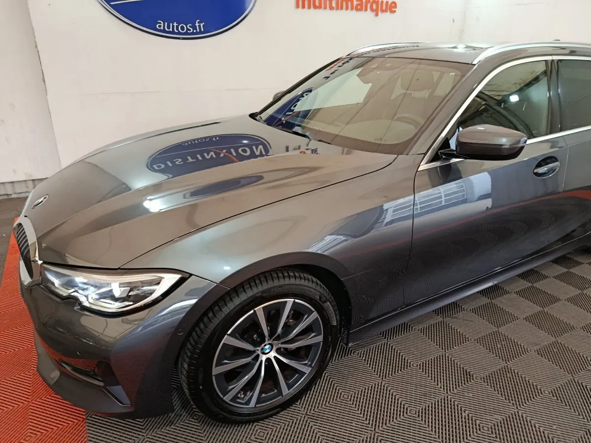 BMW Série 3 318d gris clair vue 3/4 avant droit, mettant en valeur ses phares LED et jantes alliage.