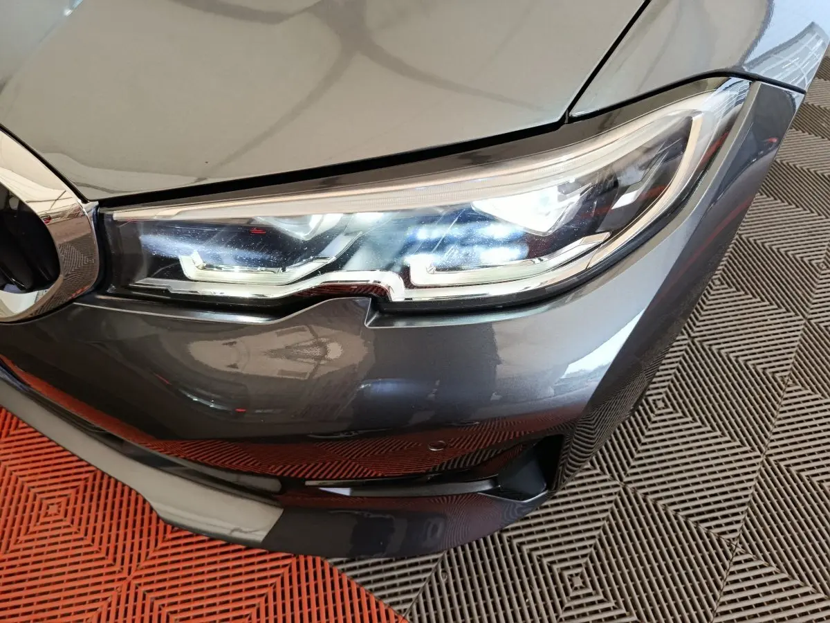 Gros plan sur le phare avant droit d'une BMW Série 3 gris clair, mettant en valeur les détails LED et la calandre.