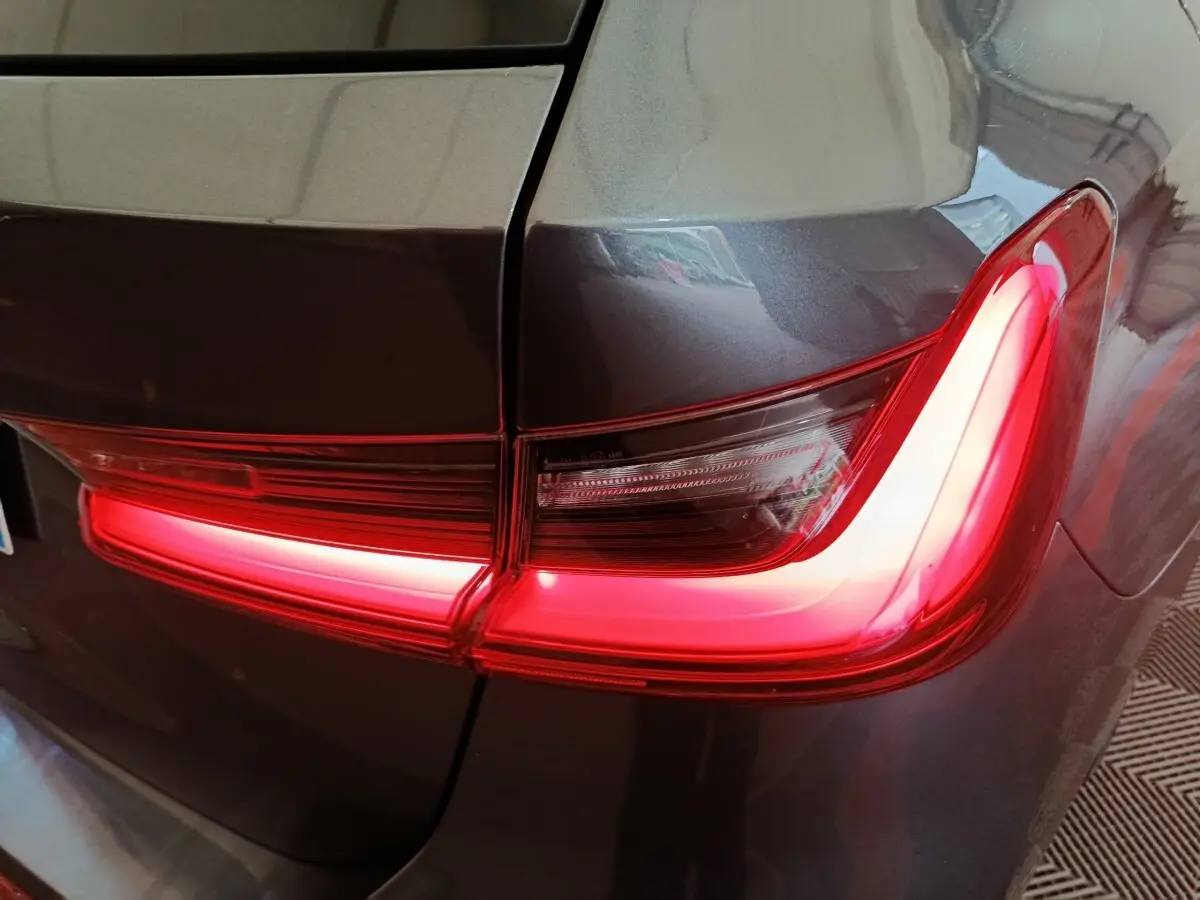 Gros plan sur le feu arrière droit rouge allumé d'une BMW Série 3 gris clair, version 318d Lounge 2022.