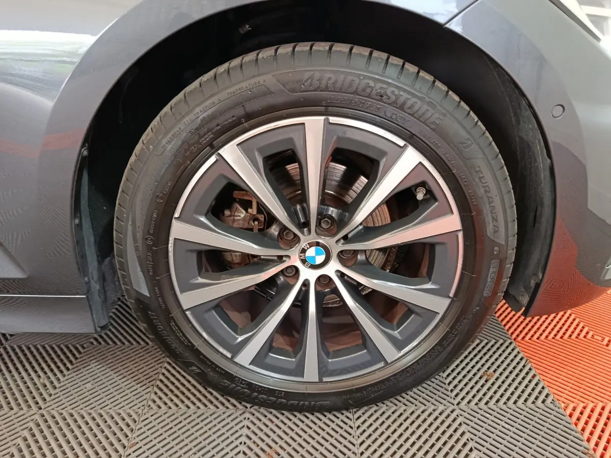 Gros plan sur la roue avant droite gris clair d'une BMW Série 3 318d avec jante alliage et logo BMW au centre.