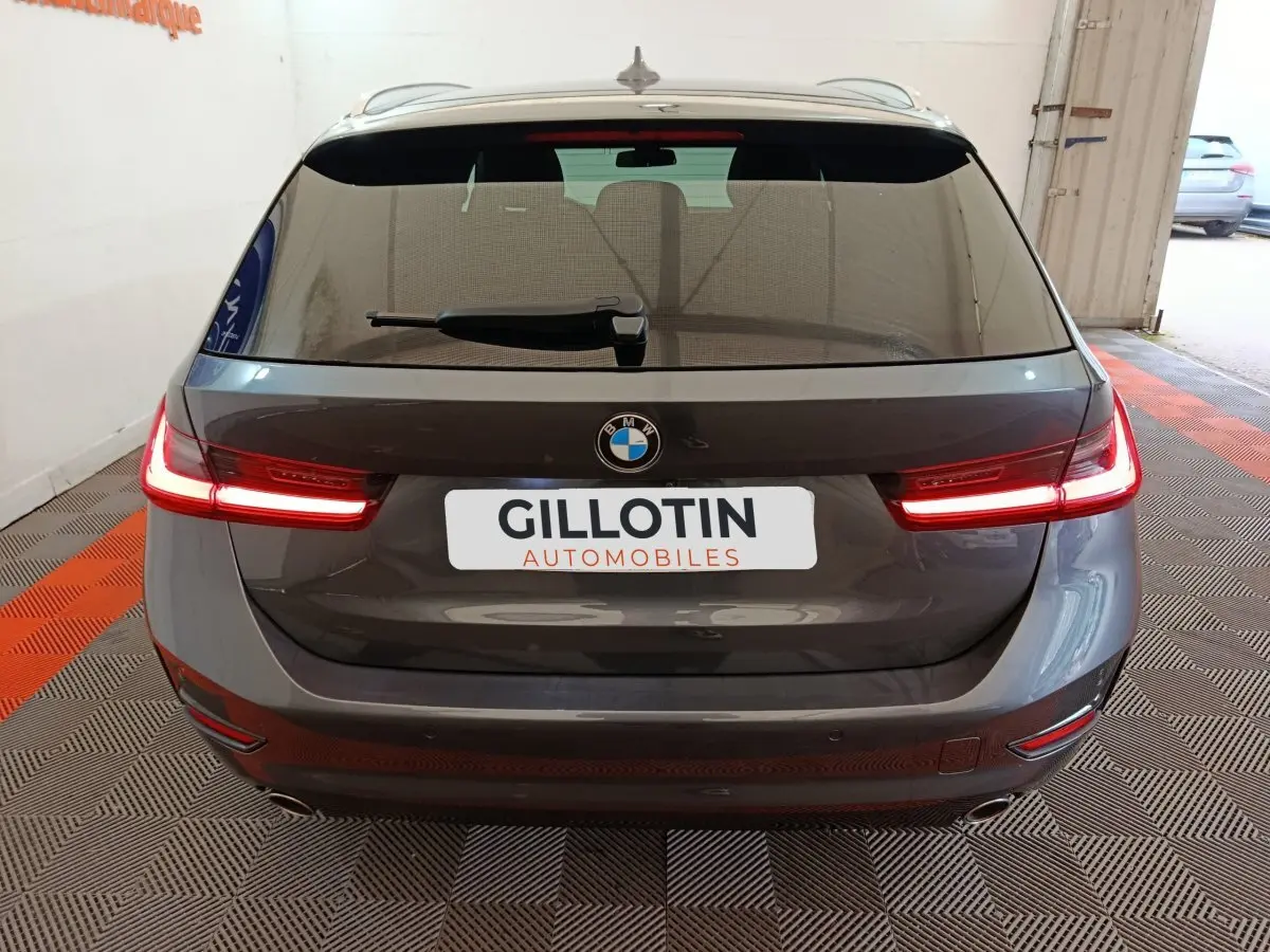 Vue arrière d'une BMW Série 3 318d gris clair avec feux LED allumés dans un garage.