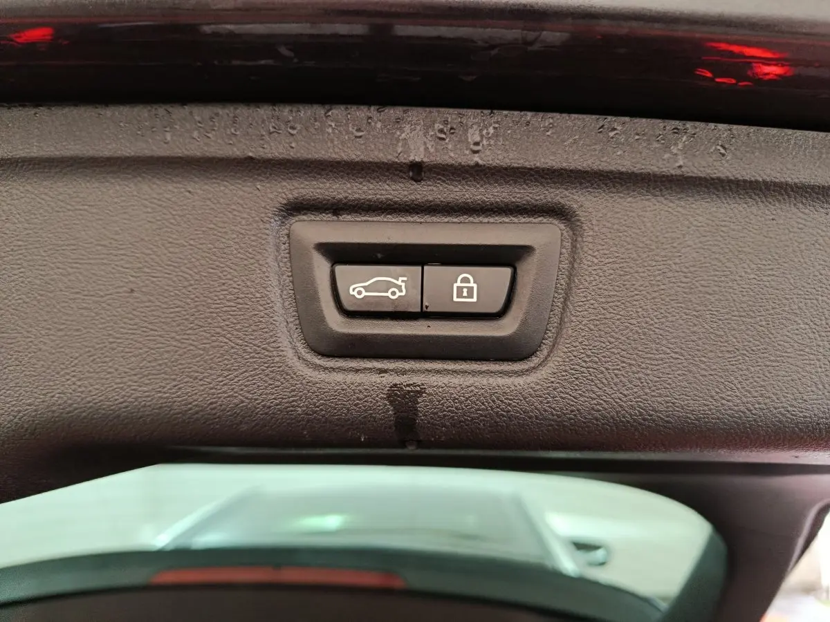Gros plan sur les boutons d'ouverture et de verrouillage du coffre sur le hayon d'une BMW Série 3 gris clair.