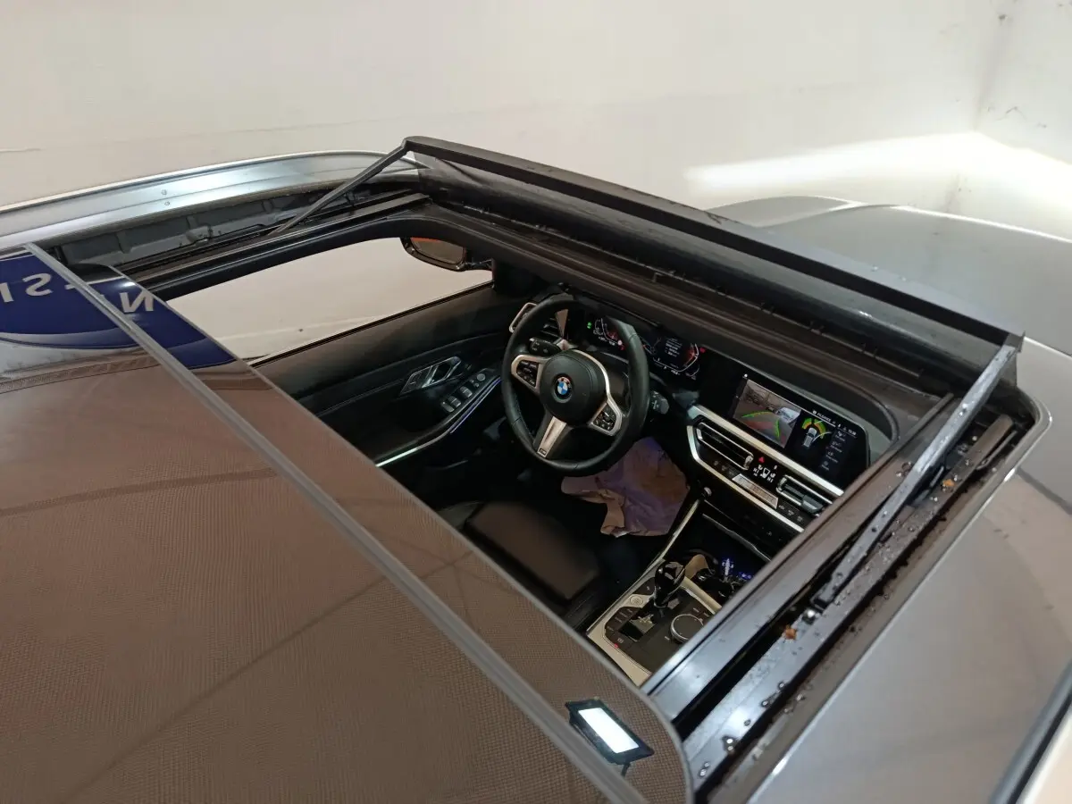 Vue plongeante sur l'intérieur noir d'une BMW Série 3 318d gris clair, avec toit ouvrant et tableau de bord digital.