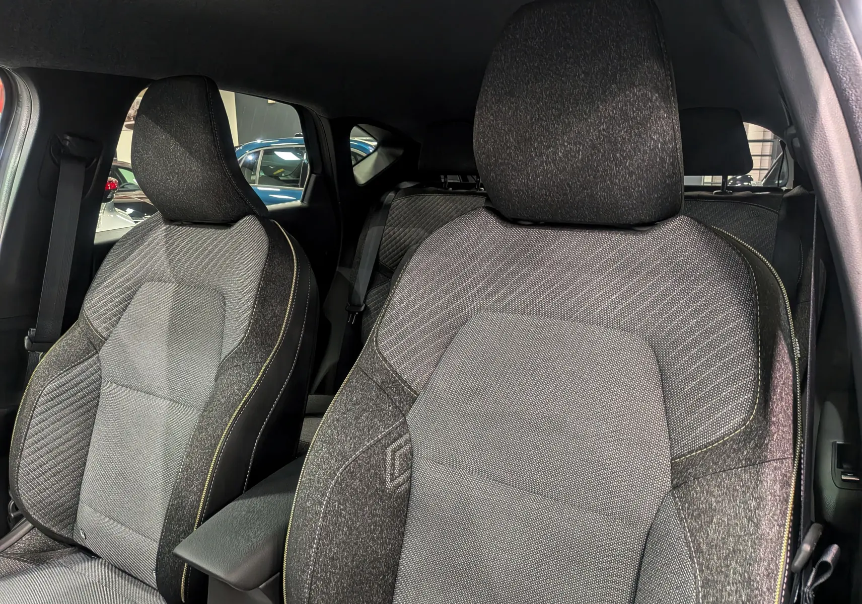 Gros plan sur les sièges avant en tissu gris du Renault Captur Mild Hybrid 2025, avec surpiqûres jaunes visibles.