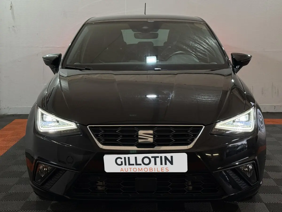 Vue frontale d'une SEAT Ibiza 1.0 TSI 110 FR noire avec phares LED allumés dans un showroom.