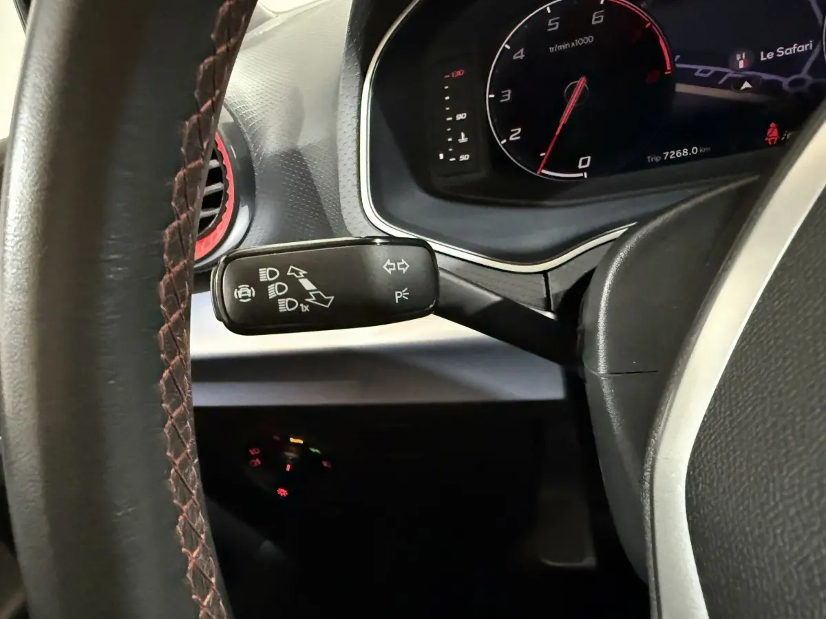 Gros plan sur le commodo gauche du volant cuir alu de la SEAT IBIZA 1.0 TSI 110 FR noir, avec tableau de bord numérique visible.