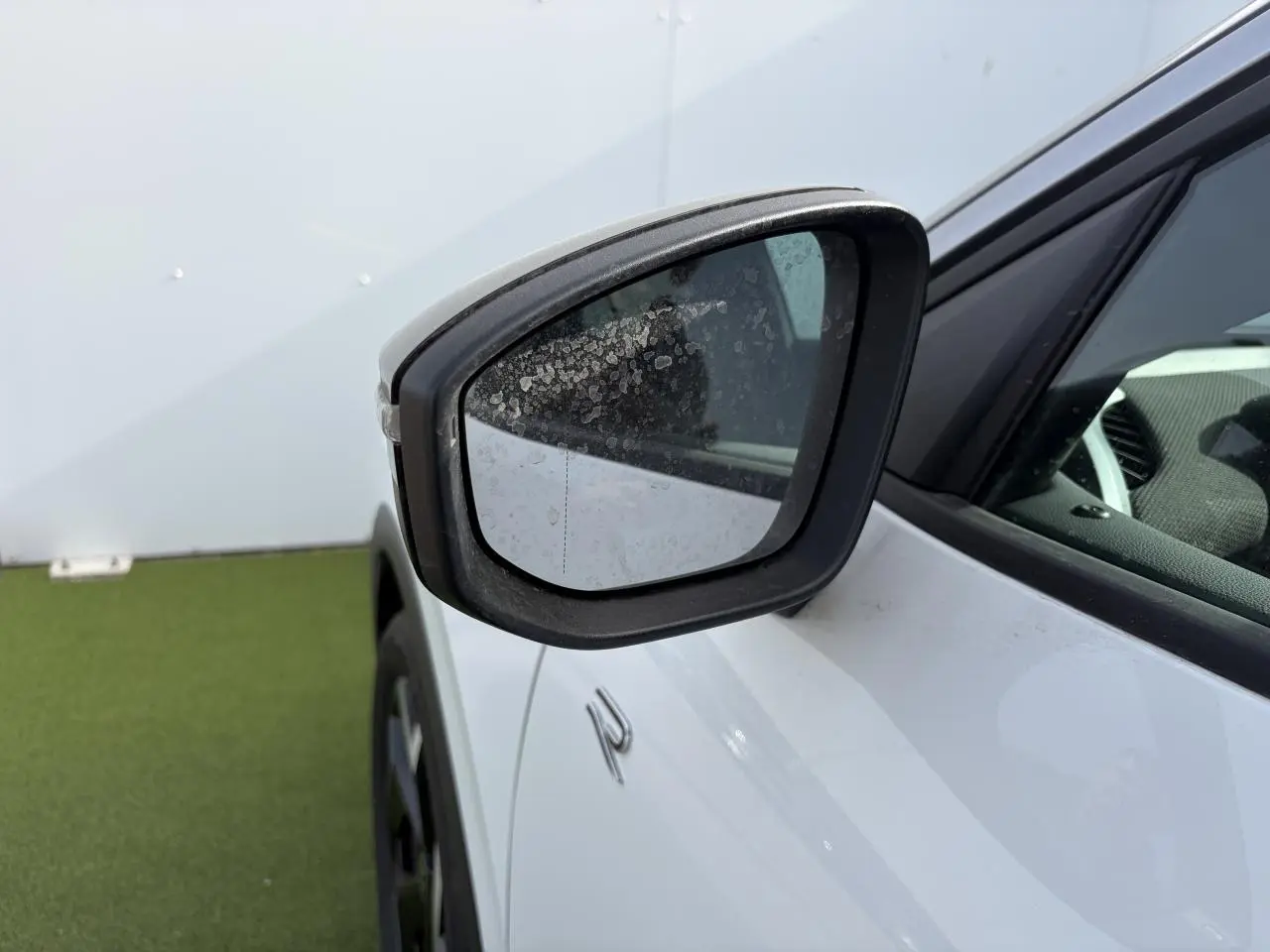 Rétroviseur côté gauche noir sur Volkswagen T-Roc blanc pur avec logo R-Line visible en gros plan.