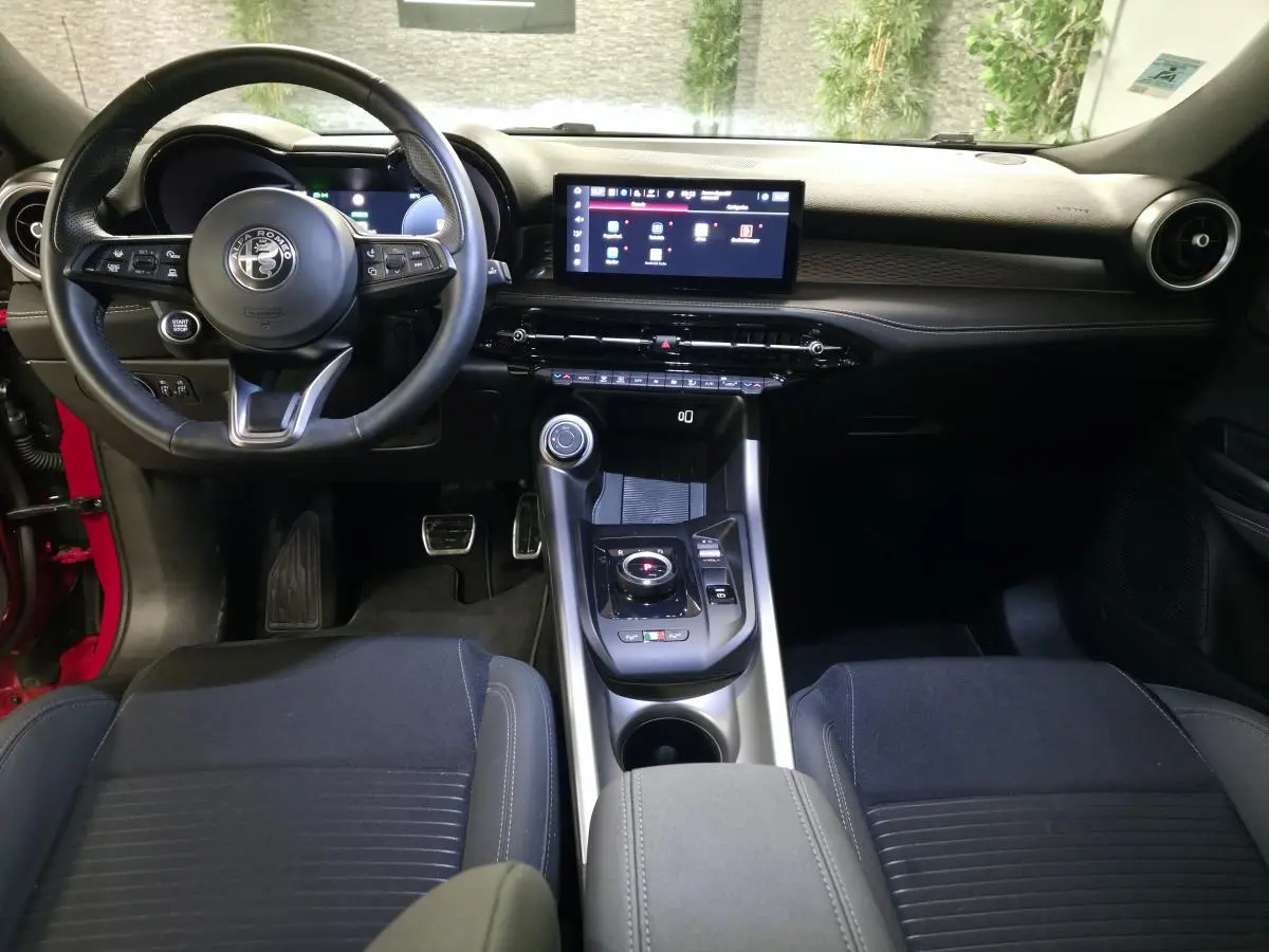 Vue intérieure avant de l'Alfa Romeo Tonale rouge 2025, avec tableau de bord noir et écran tactile central.