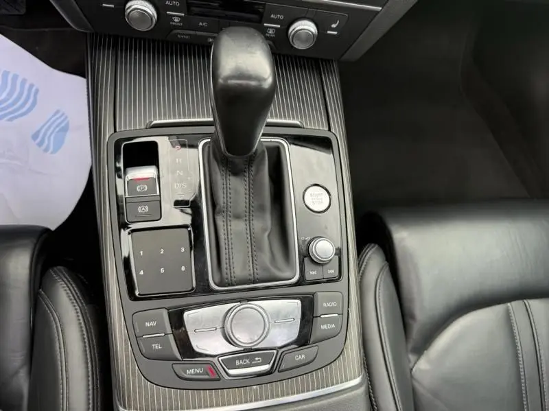 Vue rapprochée de la console centrale noire de l'Audi A7 Sportback blanche, mettant en valeur le levier de vitesse et les commandes multimédia.