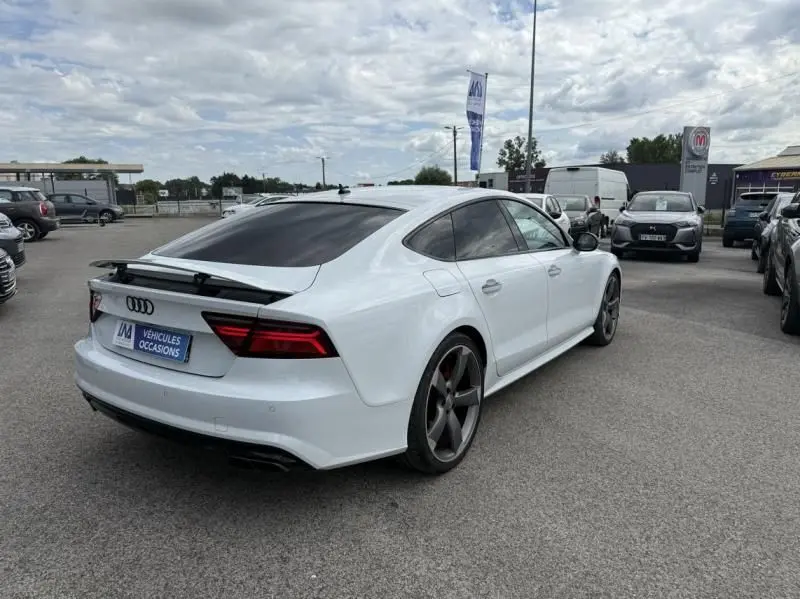 Audi A7 Sportback blanc vue 3/4 arrière droit, avec aileron arrière déployé et jantes foncées distinctives.